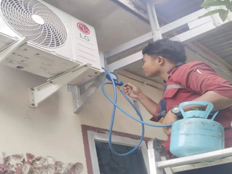 Teknisi mengisi refrigeran pada unit outdoor AC menggunakan tabung gas